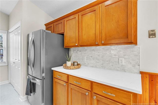 kitchen with brown cabinetry, decorative backsplash, stainless steel fridge with ice dispenser, and light countertops