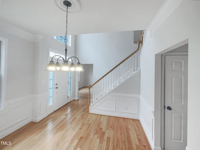 entrance foyer with a decorative wall, stairway, a wainscoted wall, light wood-style floors, and a notable chandelier