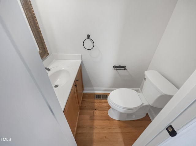 half bathroom featuring visible vents, baseboards, toilet, wood finished floors, and vanity