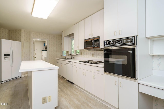 kitchen with a sink, wallpapered walls, a center island, white appliances, and light countertops