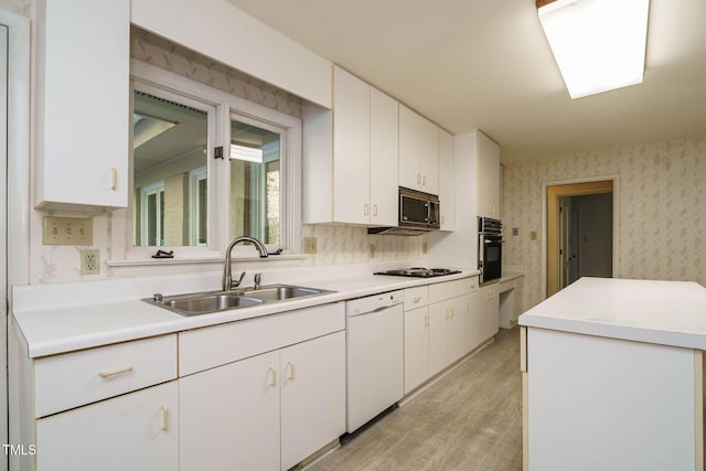 kitchen with wallpapered walls, white dishwasher, a sink, stainless steel microwave, and black oven