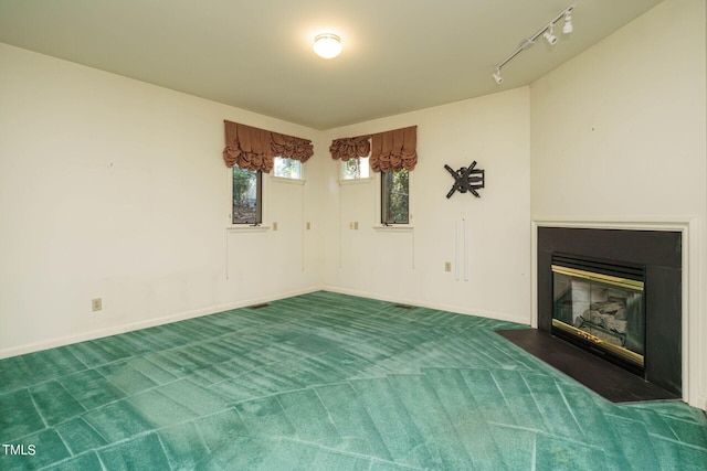 unfurnished living room with a fireplace with flush hearth, rail lighting, baseboards, and carpet