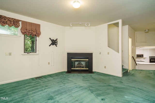 unfurnished living room with baseboards, carpet floors, a fireplace with flush hearth, stairs, and rail lighting