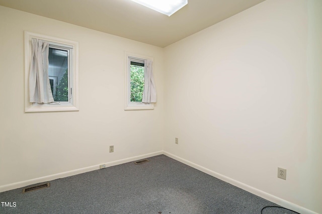 spare room with dark colored carpet, visible vents, and baseboards