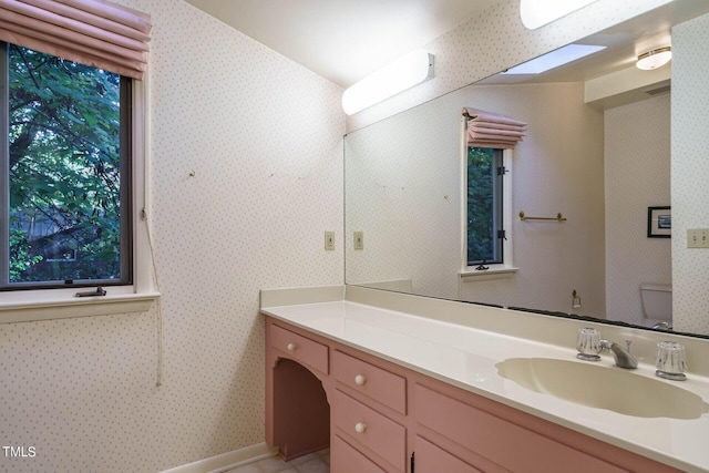 bathroom featuring toilet, a healthy amount of sunlight, vanity, and wallpapered walls