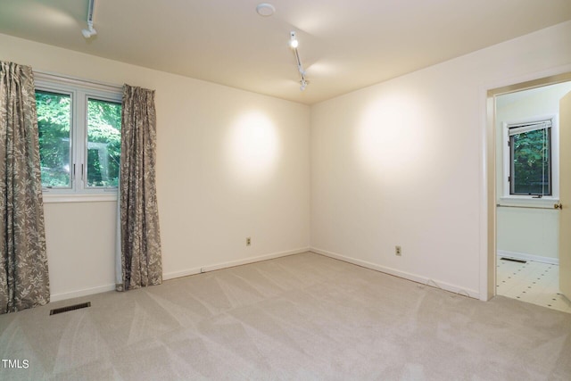 empty room with track lighting, carpet, visible vents, and baseboards