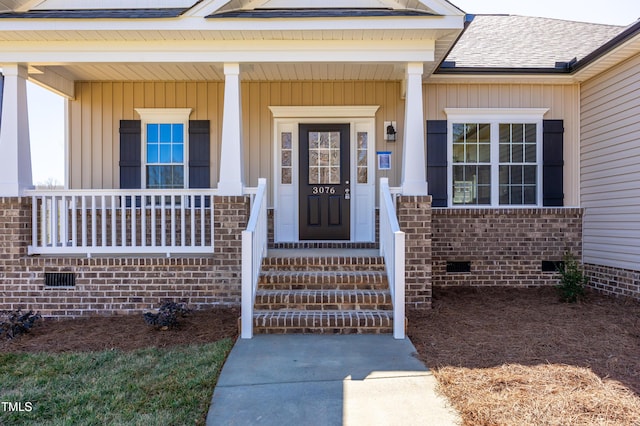 view of exterior entry featuring crawl space, brick siding, a porch, and a shingled roof