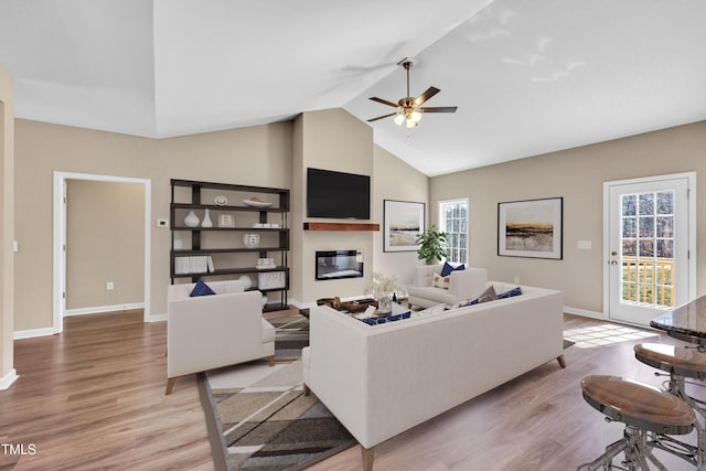 living area featuring a glass covered fireplace, baseboards, light wood finished floors, and high vaulted ceiling