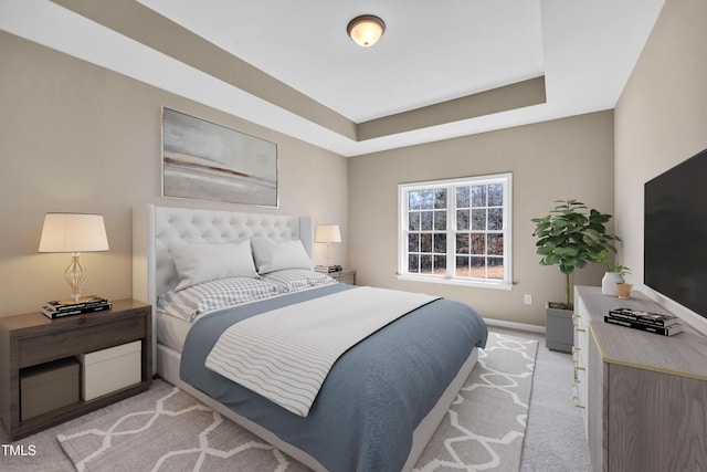 bedroom featuring light colored carpet, a raised ceiling, and baseboards