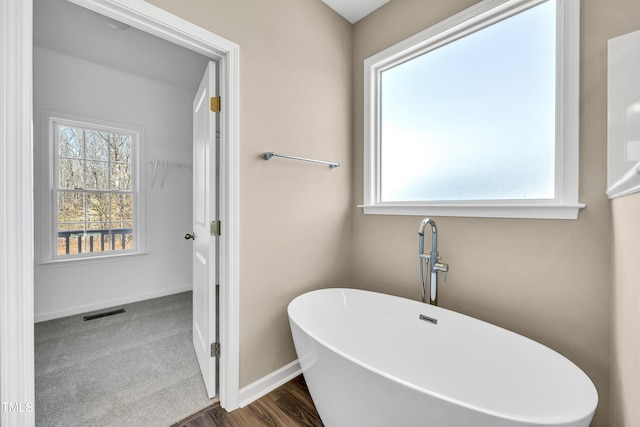 full bathroom featuring a soaking tub, plenty of natural light, baseboards, and visible vents