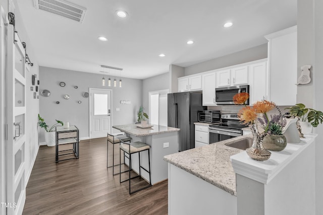 kitchen with visible vents, a kitchen island, a breakfast bar, appliances with stainless steel finishes, and a barn door