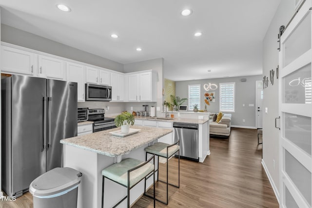 kitchen featuring a sink, wood finished floors, white cabinetry, appliances with stainless steel finishes, and a peninsula