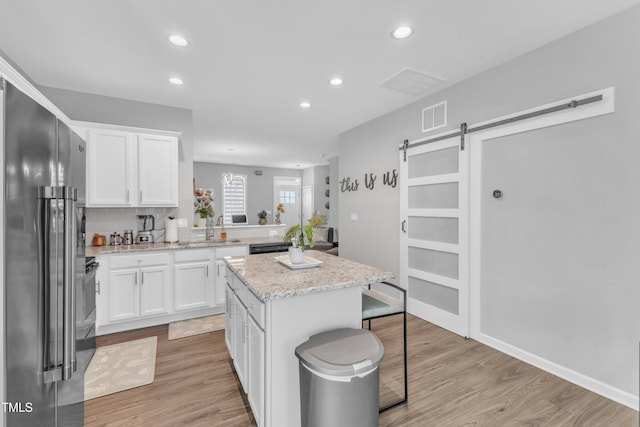 kitchen with visible vents, a kitchen island, a barn door, high end refrigerator, and a sink