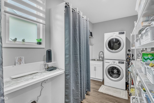 laundry room featuring wood finished floors, stacked washer / dryer, cabinet space, and a sink