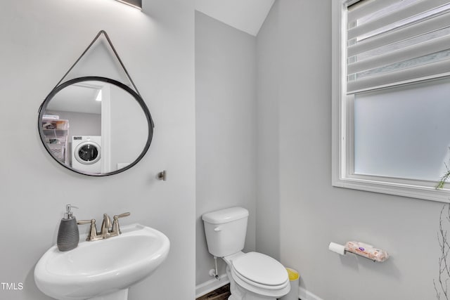 half bath featuring a sink, baseboards, washer / clothes dryer, and toilet