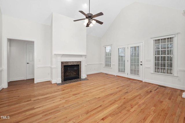 unfurnished living room with light wood-type flooring, high vaulted ceiling, a ceiling fan, a premium fireplace, and baseboards