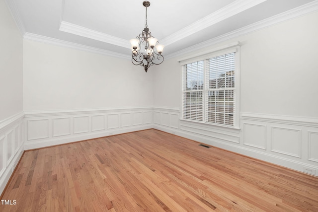 spare room featuring visible vents, wainscoting, light wood-style flooring, an inviting chandelier, and a raised ceiling