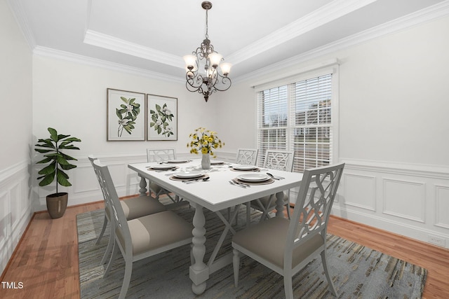 dining space with a tray ceiling, light wood-style flooring, a notable chandelier, and a wainscoted wall