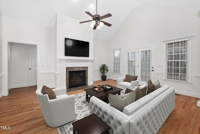 living room with ceiling fan, light wood-style flooring, a fireplace, and high vaulted ceiling