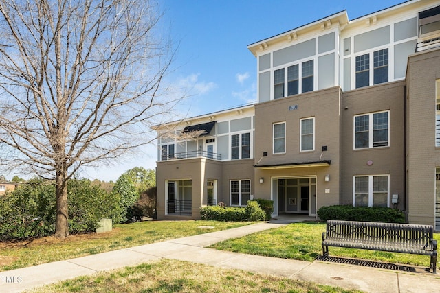 multi unit property with brick siding, a balcony, and a front lawn