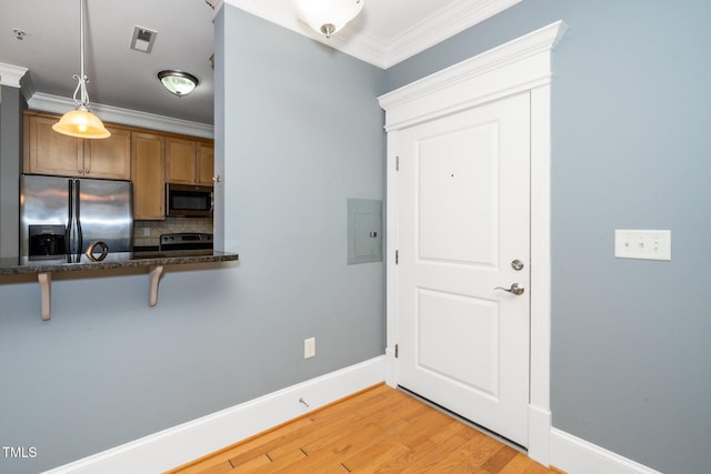 kitchen featuring a breakfast bar area, ornamental molding, decorative backsplash, appliances with stainless steel finishes, and brown cabinets