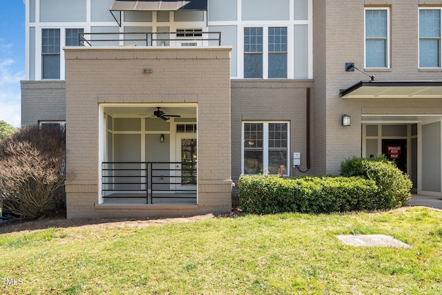 entrance to property featuring a ceiling fan, a lawn, and brick siding