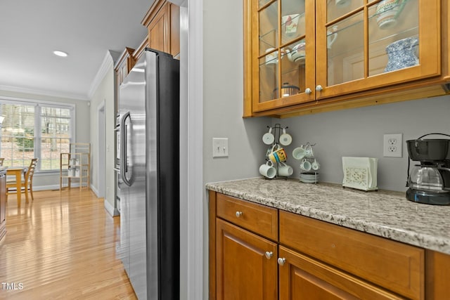 kitchen featuring light stone counters, brown cabinetry, freestanding refrigerator, and ornamental molding