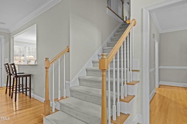 stairway with wood finished floors, baseboards, and ornamental molding