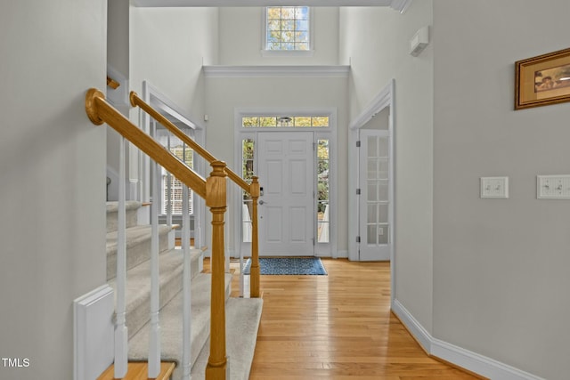 foyer entrance featuring stairway, baseboards, a high ceiling, and light wood finished floors