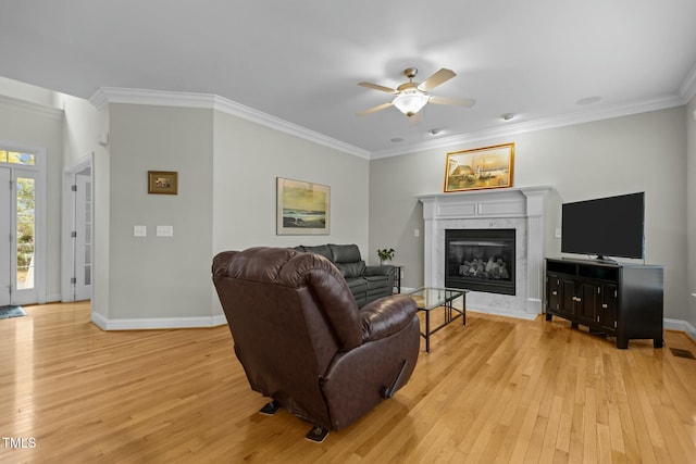 living room featuring a high end fireplace, crown molding, baseboards, light wood-style flooring, and a ceiling fan