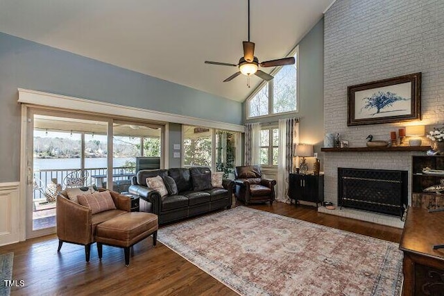 living area with wood finished floors, high vaulted ceiling, a fireplace, a water view, and wainscoting