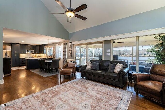 living area with dark wood finished floors, ceiling fan with notable chandelier, a water view, and high vaulted ceiling