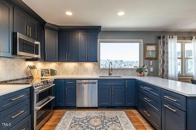 kitchen featuring a sink, blue cabinetry, stainless steel appliances, a peninsula, and light countertops