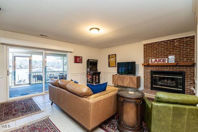 living area with crown molding, wainscoting, a fireplace, light tile patterned flooring, and a decorative wall