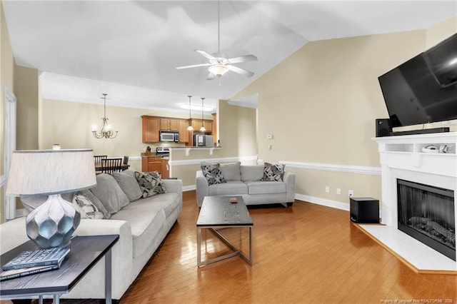 living area featuring ceiling fan with notable chandelier, wood finished floors, a fireplace, and vaulted ceiling