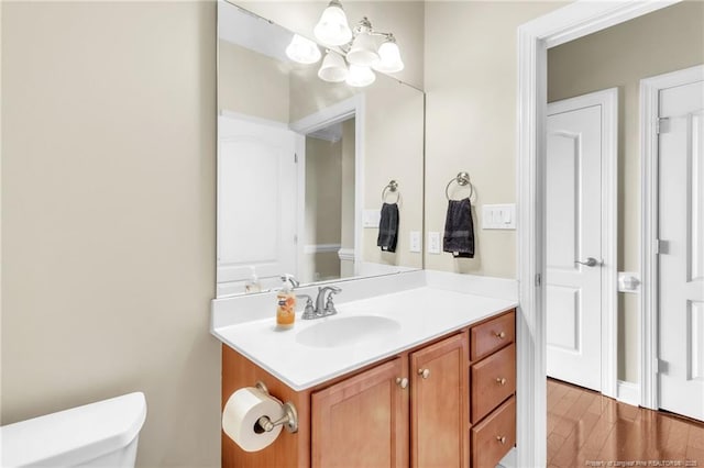 half bathroom with a notable chandelier, toilet, wood finished floors, and vanity