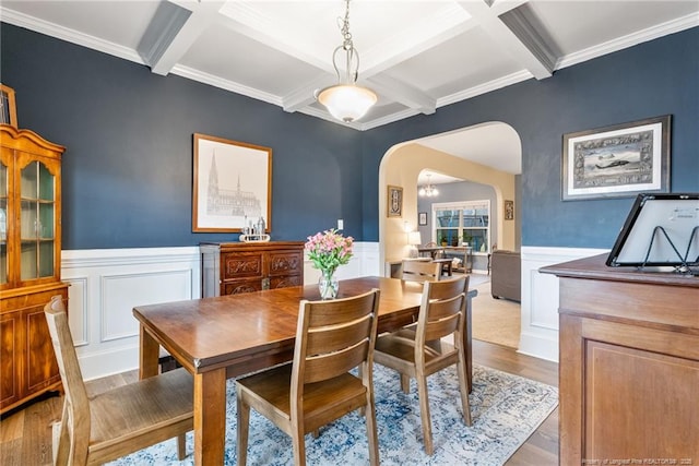 dining room featuring arched walkways, beamed ceiling, wainscoting, and wood finished floors