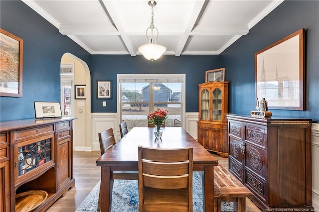 dining space featuring beam ceiling, coffered ceiling, wood finished floors, arched walkways, and wainscoting