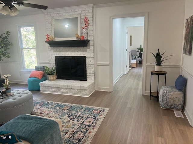 living room with crown molding, baseboards, ceiling fan, a fireplace, and wood finished floors