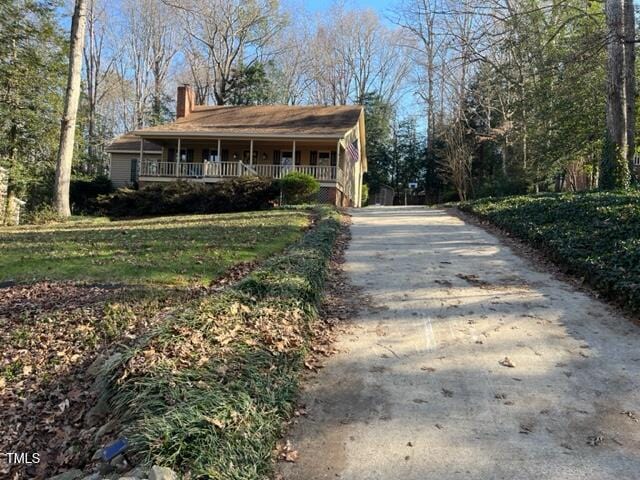 view of front facade featuring a porch, driveway, and a chimney