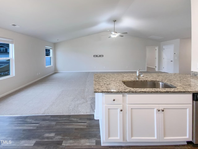 kitchen featuring open floor plan, light stone countertops, white cabinetry, and a sink