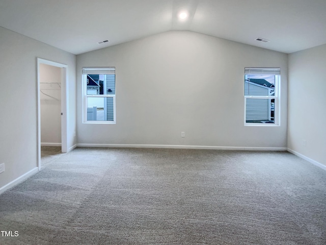 unfurnished bedroom featuring visible vents, a walk in closet, carpet, and vaulted ceiling