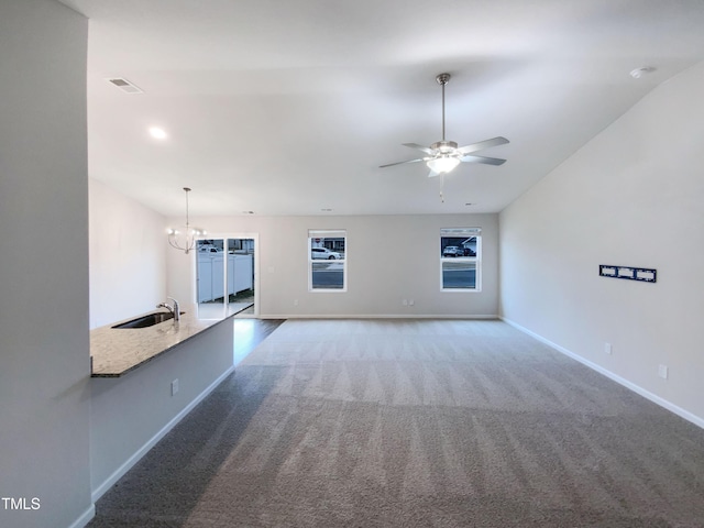 unfurnished living room featuring baseboards, visible vents, a sink, carpet flooring, and ceiling fan with notable chandelier