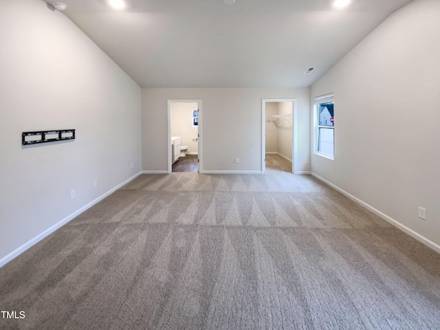 unfurnished bedroom featuring connected bathroom, carpet flooring, baseboards, a spacious closet, and vaulted ceiling