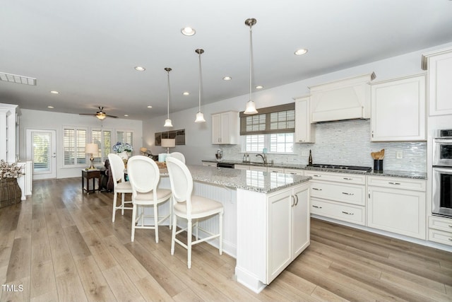 kitchen featuring premium range hood, visible vents, light wood-type flooring, and appliances with stainless steel finishes