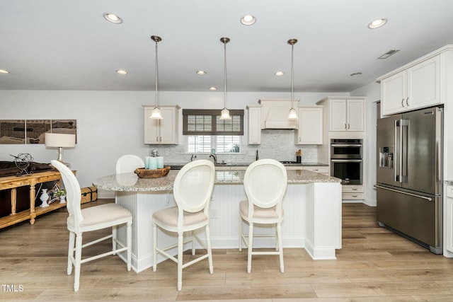 kitchen featuring premium range hood, stainless steel appliances, light stone countertops, and light wood-style flooring