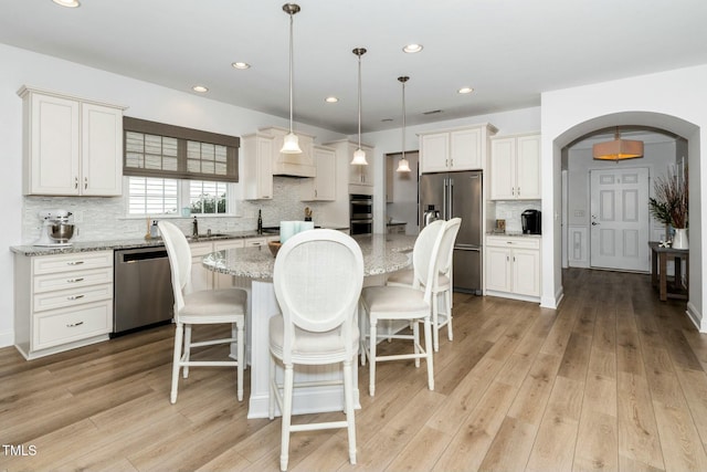 kitchen with light wood finished floors, a kitchen island, a breakfast bar, arched walkways, and appliances with stainless steel finishes