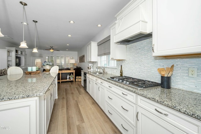 kitchen featuring premium range hood, light wood-type flooring, stainless steel gas stovetop, and white cabinets