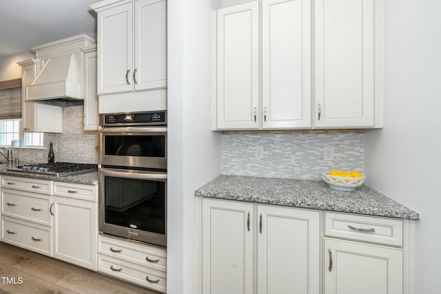 kitchen featuring decorative backsplash, custom range hood, light stone countertops, and appliances with stainless steel finishes