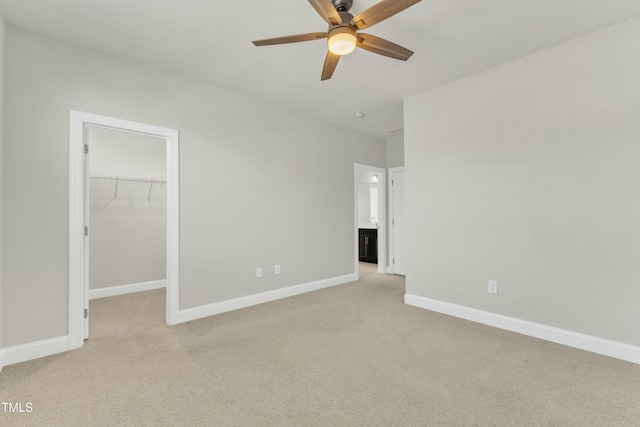 unfurnished bedroom featuring a walk in closet, baseboards, light carpet, a closet, and a ceiling fan